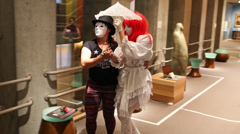 Two masked characters walk under an umbrella