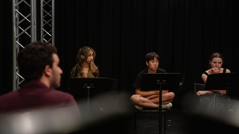 3 people sitting behind music stands listening to something off camera