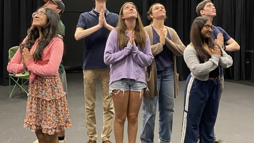 Eight students standing in a circle, facing out, with hands together in a prayer.